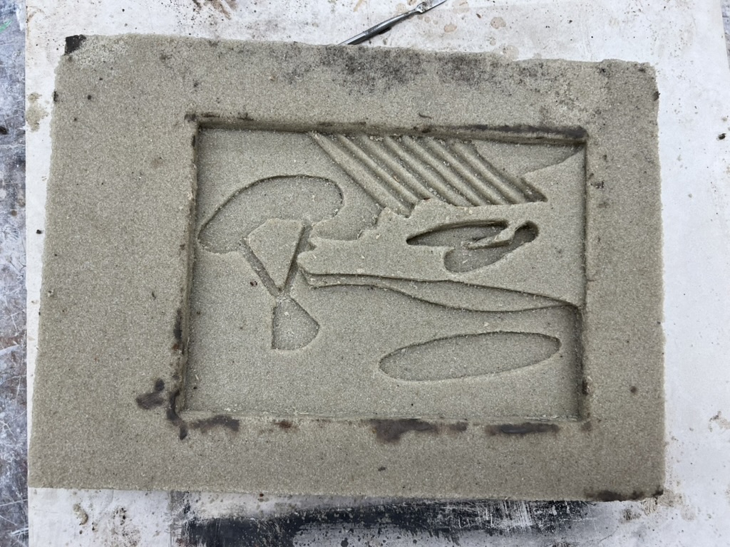 Sand mold cavity with the relief design impressed for aluminum pour
