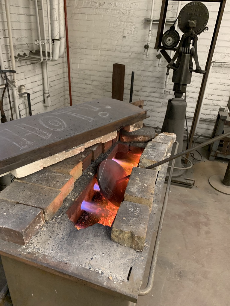Custom metal branding iron heating in a firebrick forge with flames