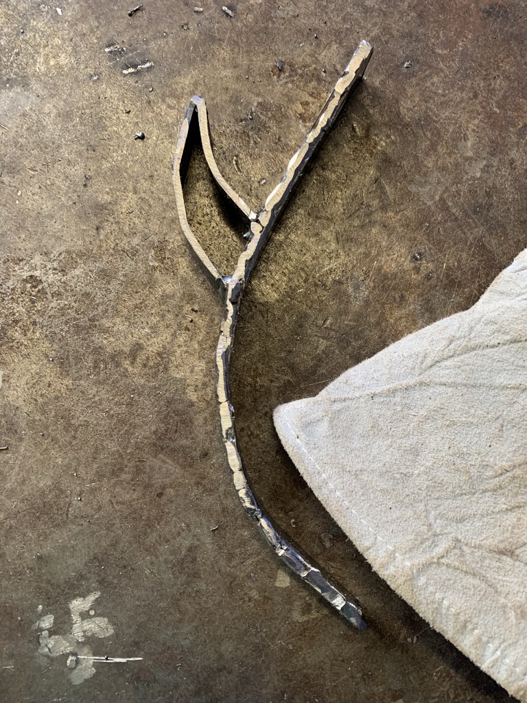 Cut and welded leaf-shaped steel piece next to a welding glove